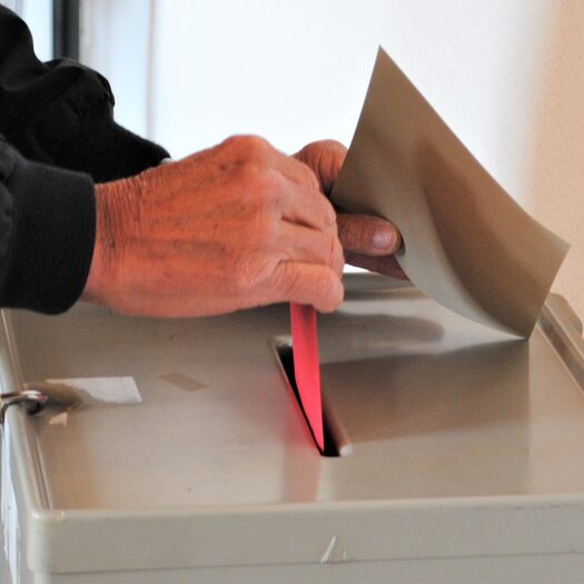 Hand schmeißt roten Umschlag mit Wahlschein in die Wahlurne