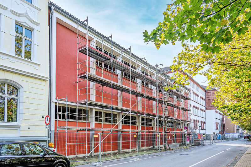 Blick auf die eingerüstete Turnhalle des Ganztagsgymnasiums Johannes Rau mit dem Altbau der Schule dahinter