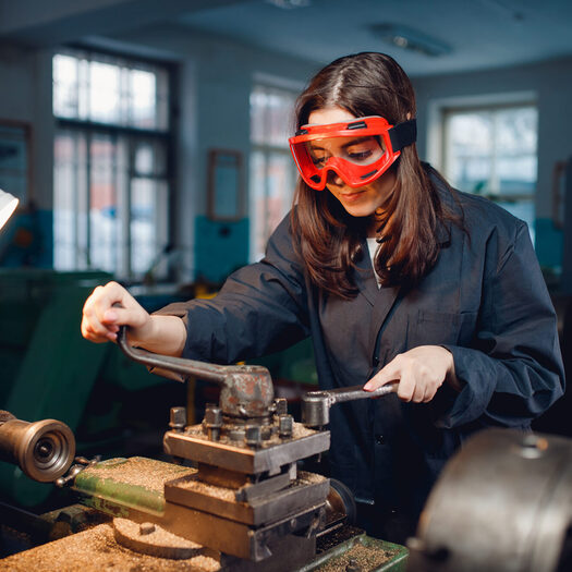 Young woman student works on an automatic lathe CNC, industrial workshop. Concept vocational education turner.