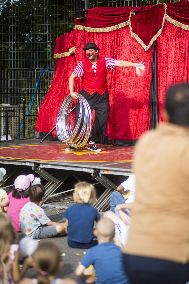 Clown mit Hula-Hoops und sitzenden Kindern im Vordergrund