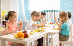 Gruppe Kinder sitzt essend und trinkend an kleinen Tischen