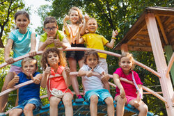 Kleinkinder sitzen auf einem Klettergerüst und winken in die Kamera