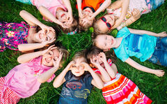 Gruppe Kinder liegt auf dem Rücken auf dem Gras, formt mit Fingern Ferngläser auf den Augen