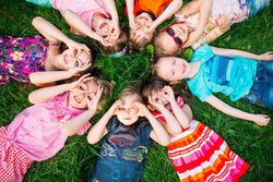 Gruppe Kinder liegt auf dem Rücken auf dem Gras, formt mit Fingern Ferngläser auf den Augen