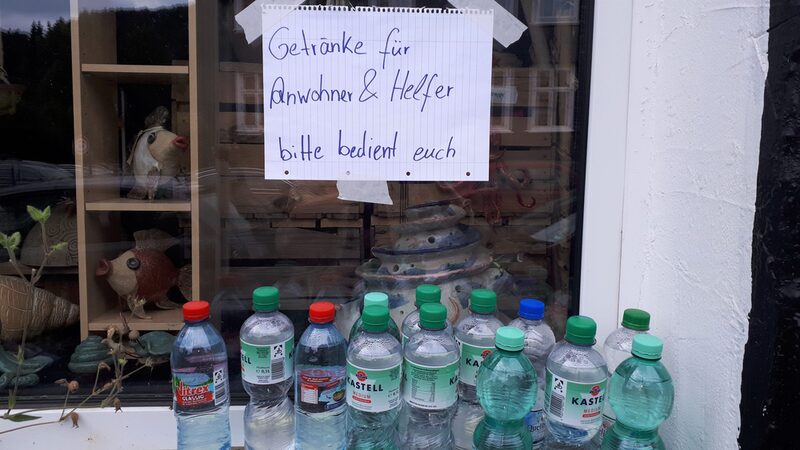 Mineralwasserflaschen auf einer Fensterbank mit dem Schild "Getränke für Anwohner & Helfer - bitte bedient euch"