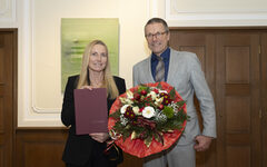 Dr. Sandra Zeh mit Urkundenmappe neben Oberbürgermeister Uwe Schneidewind mit Blumenstrauß