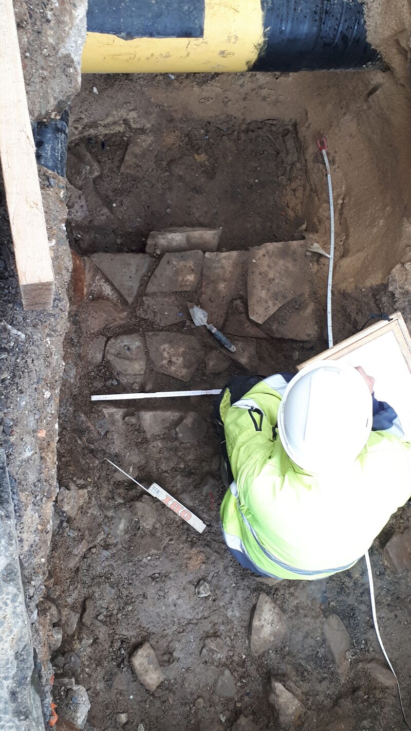 Burgmauerrest in einer Baugrube, Archäologe mit Helm und gelber Jacke