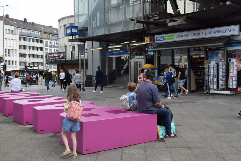 Menschen sitzen auf dem Schriftzug "Barmen" vor der Schwebebahnhaltestelle Alter Markt