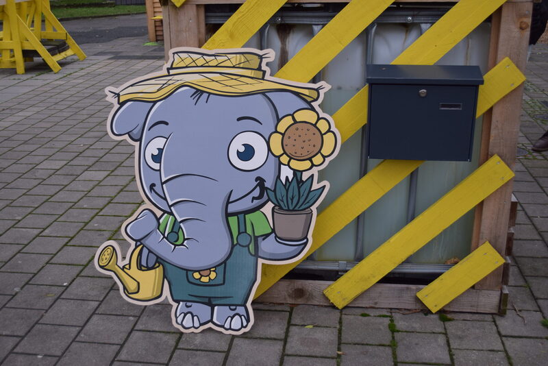 Ein Elefant mit Gieskanne und Sonnenblume als Aufsteller