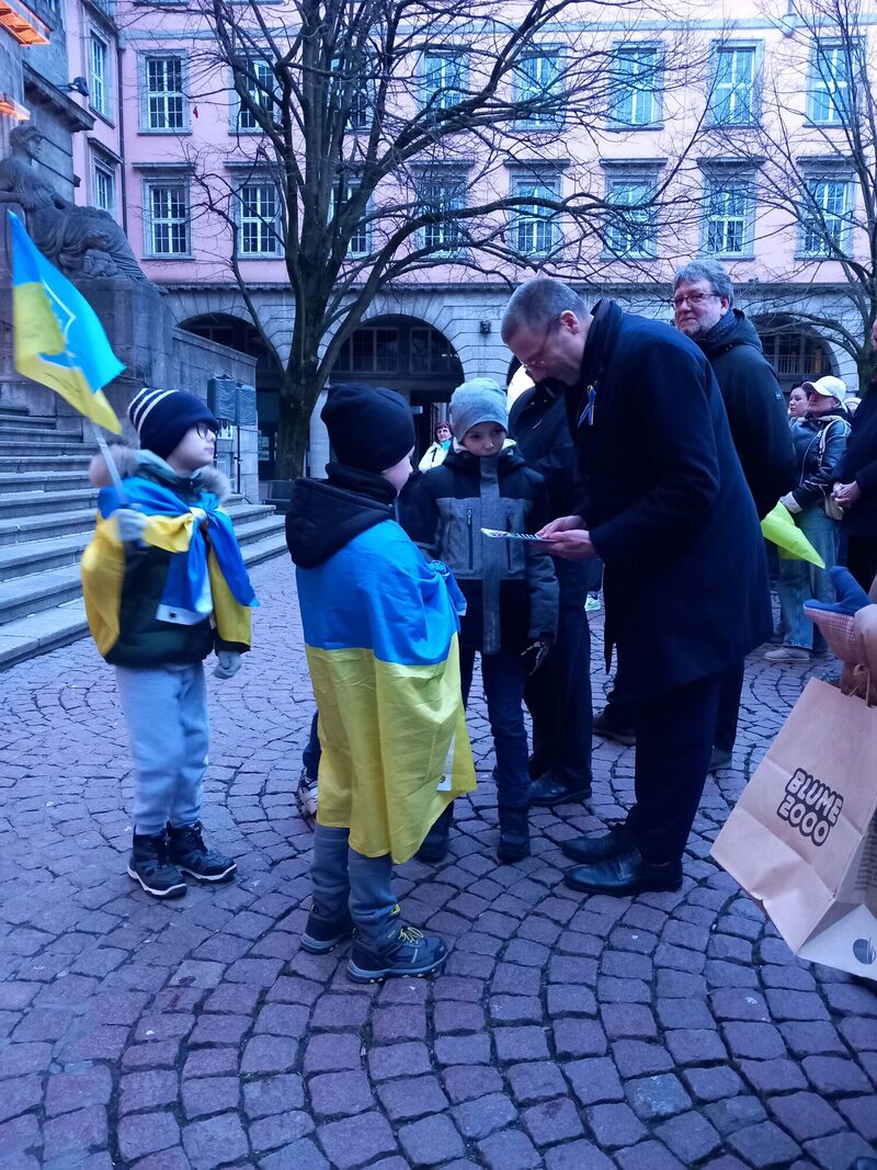 Oberbürgermeister Uwe Schneidewind nimmt Fotos der Kriegsfolgen von ukrainischen Junngen entgegen.