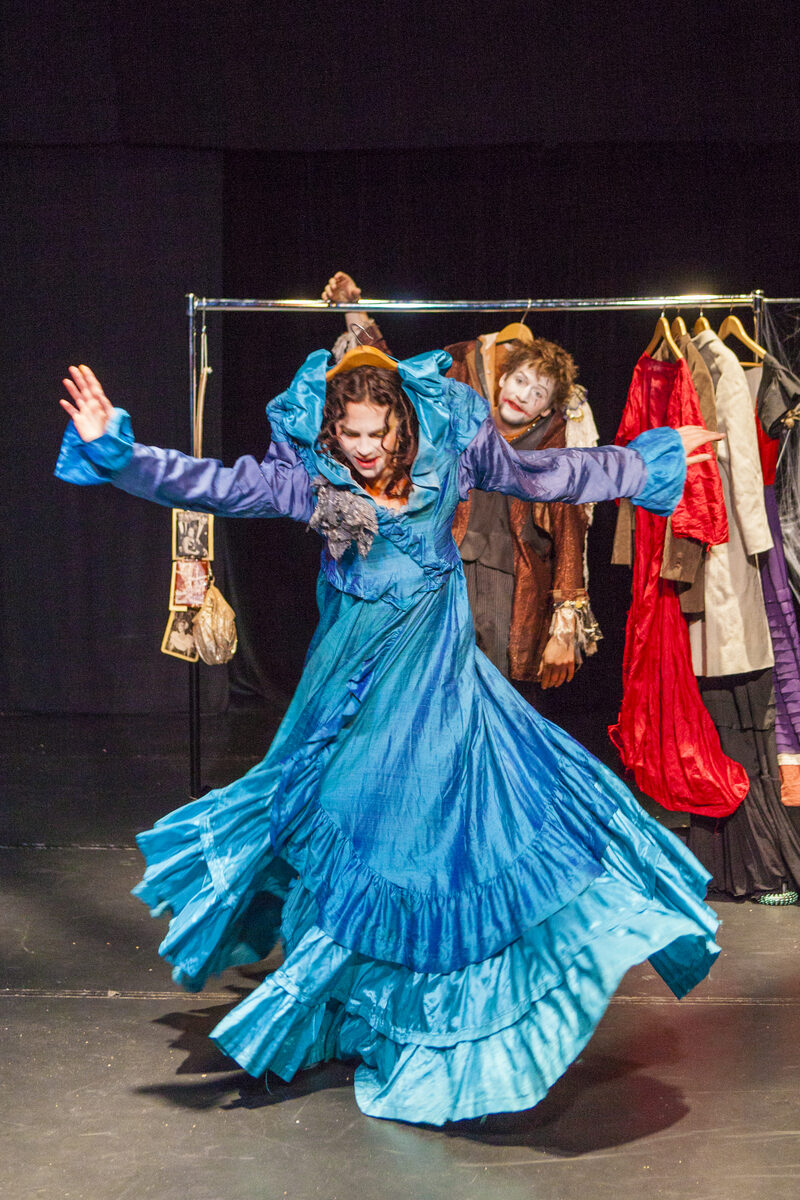 Eine Schauspielerin in einem langen blauen Kleid und ein Schauspieler dahinter