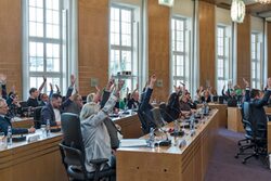 Abstimmung im Ratssaal: Stadtverordnete in Tischreihen sitzend mit erhobenen Armen