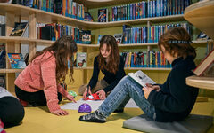 3 Mädchen sitzen auf dem Boden umringt von Bücherregalen