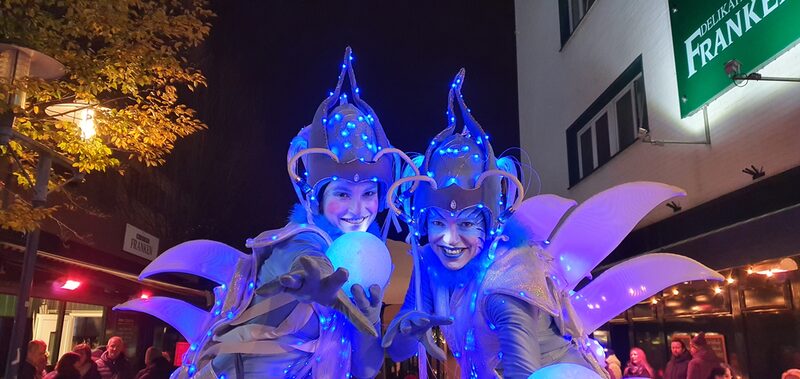 Zwei Artistinnen in blauen Lichtkostümen in der Innenstadt