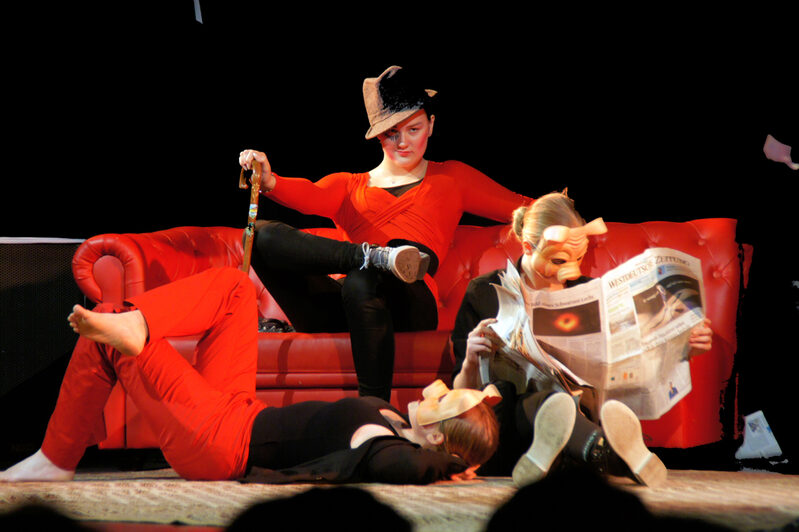 Drei Schülerinnen auf einem roten Sofa auf der Bühne, zwei tragen Schweinsmasken