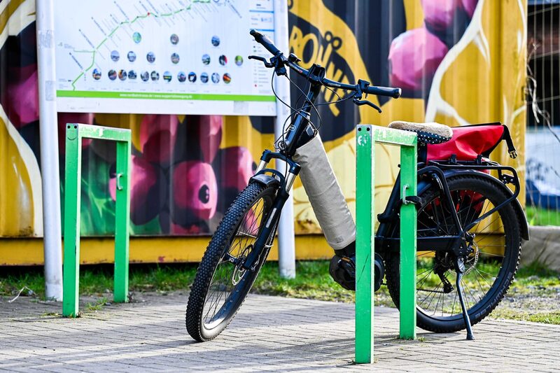 Ein Fahrrad lehnt an einem Abstell-Bügel vor einem gelben Container