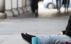 Symbolbild: Ein Mensch sitzt auf der Straße, neben ihm steht eine blaue Tasse.