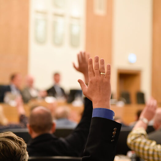 Ein Ratsmandant hebt die Hand bei einer Wahl im Ratssaal.