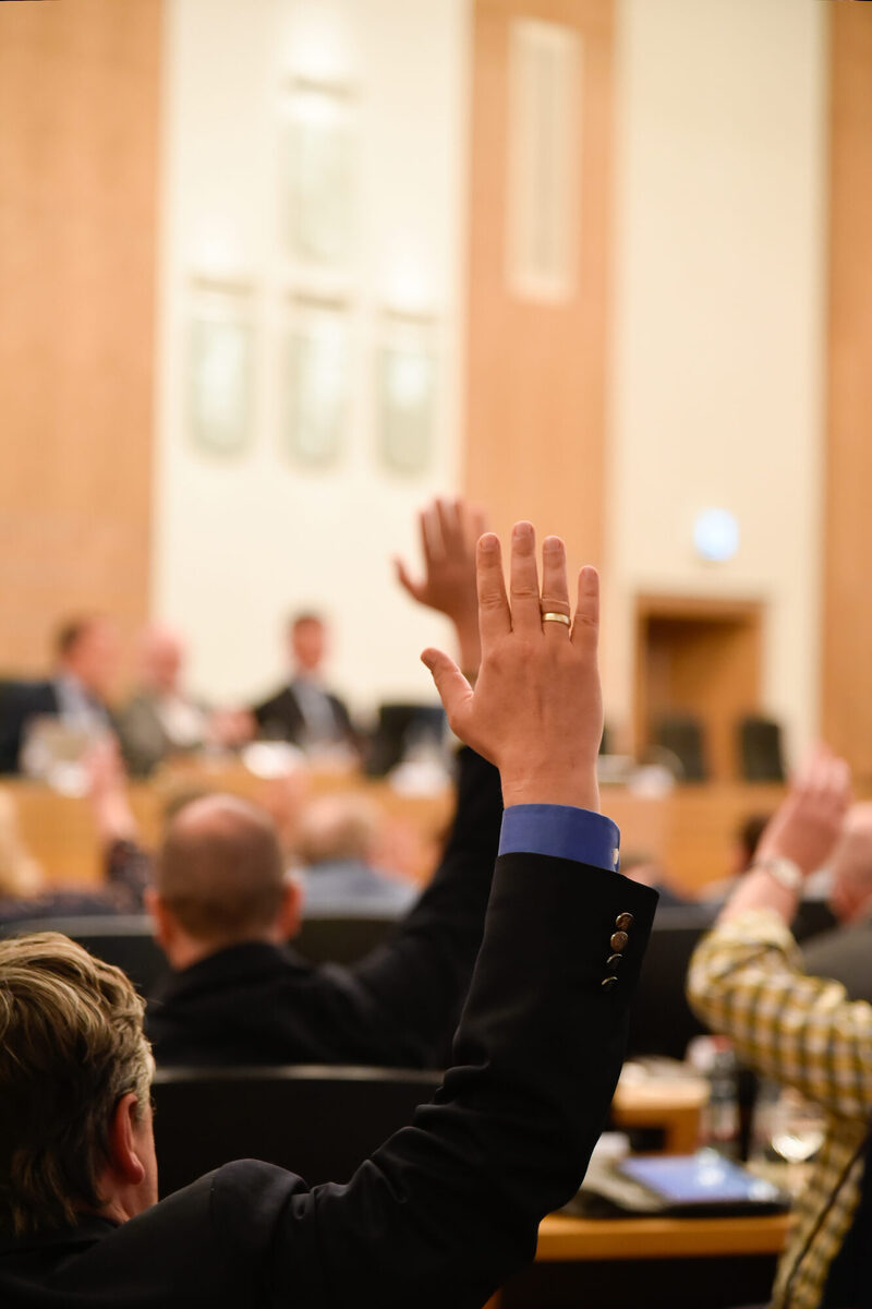 Ein Ratsmandant hebt die Hand bei einer Wahl im Ratssaal.