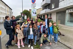 Kinder vor einem Schild das auf den autofreien Weg zur Schule hinweist mit Dezernentin Dr. Katrin Linthorst (2.v.l.)