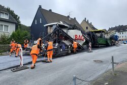 Große Asphaltiermaschine mit Arbeitern in orange-farbener Schutzkleidung