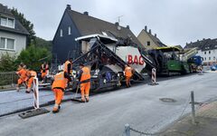 Große Asphaltiermaschine mit Arbeitern in orange-farbener Schutzkleidung