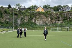 Die Sportanlage Höfen mit ihrer steilen Felswand im Hintergrund und Personen auf dem Sportplatz