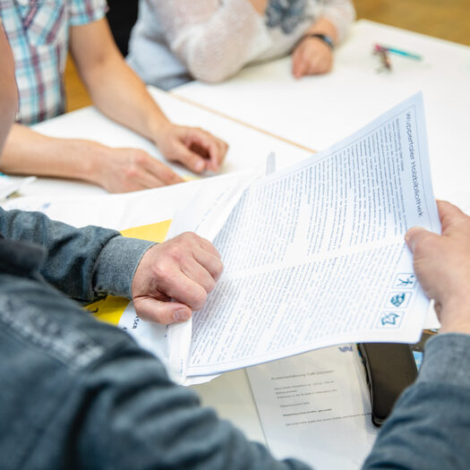 Symbolfoto des Gemeinwohlchecks: Auf einem Tisch liegen verschiedene Zettel mit Ideen. Ein Mann hält einen Zettel hoch.