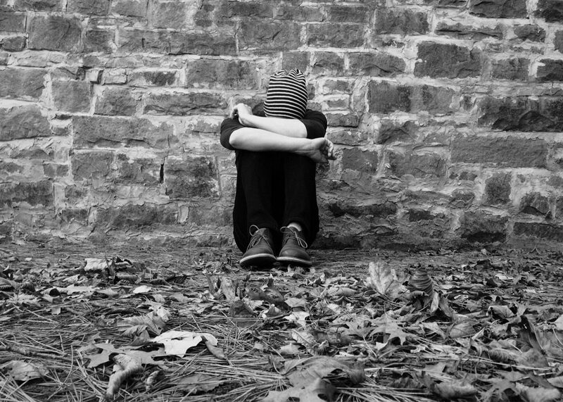 Betrübtes Kind versteckt sein Gesicht und sitzt vor einer Mauer